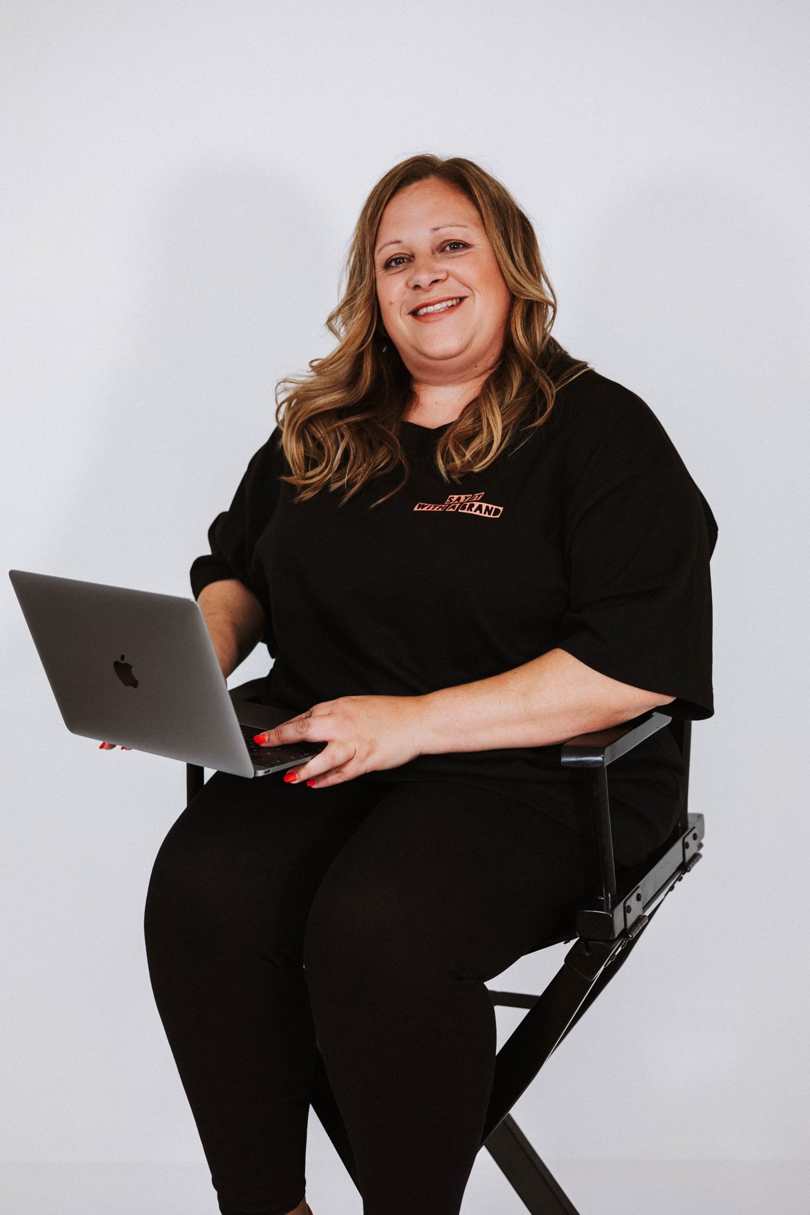 Jo on a director's chair with her laptop, smiling.