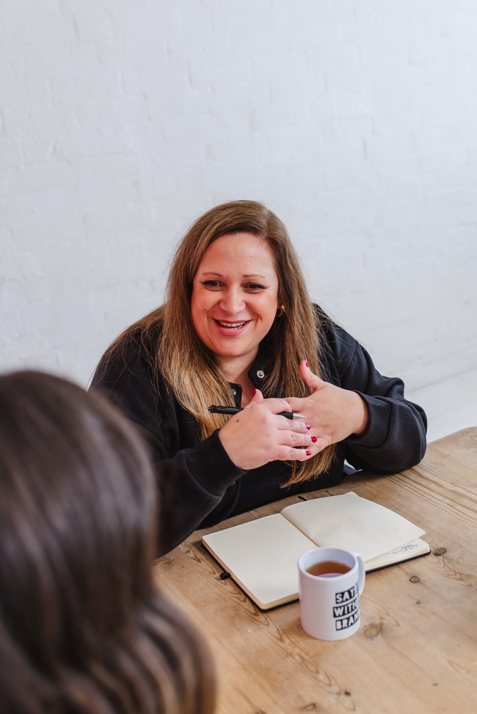 Jo talking with a client across a table, notebook and Say It With a Brand mug in front of her.