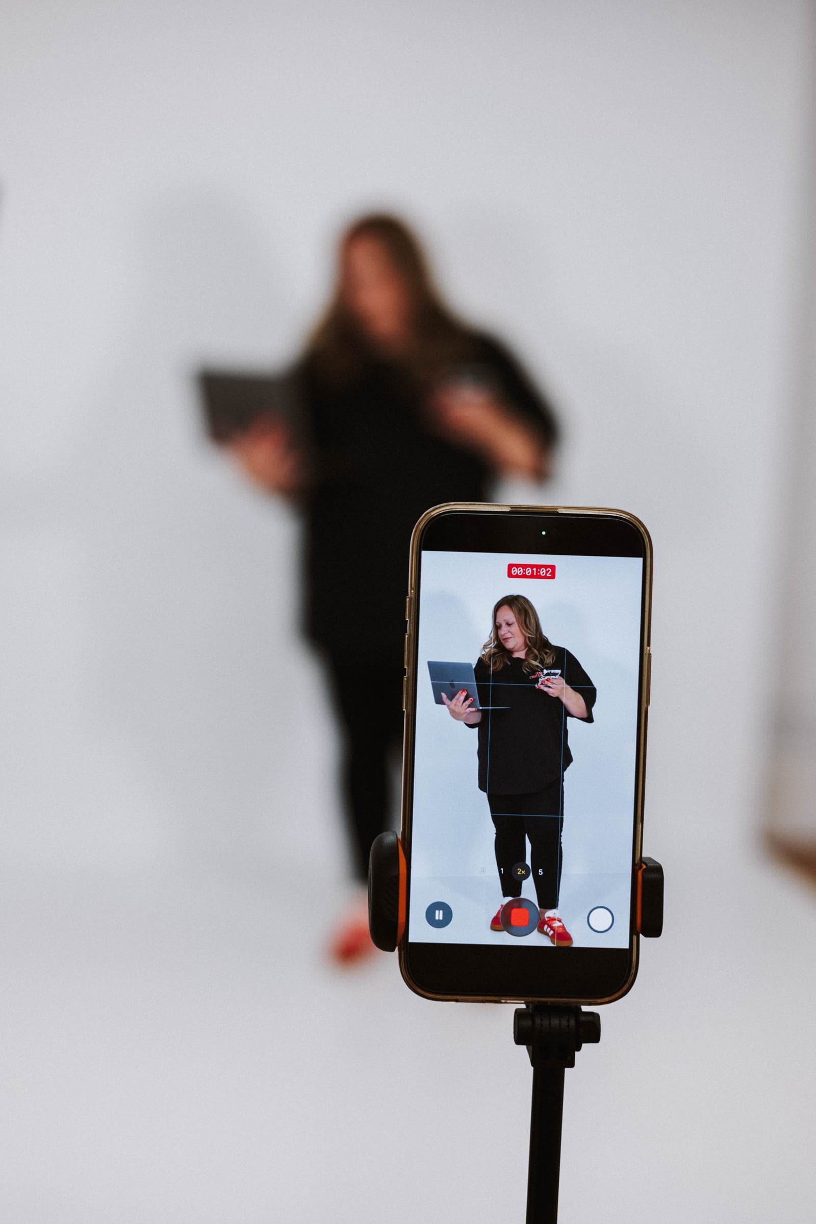 A phone on a tripod films Jo, who stands in the background.