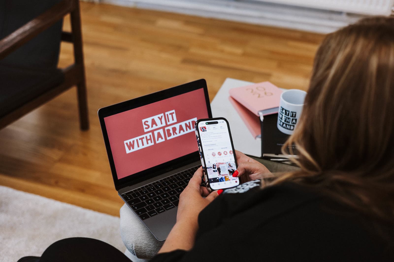A laptop showing the Say It With a Brand logo, with a phone in Jo's hand.